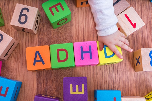 bērnu burtu klucīši, kas sakārtoti tā, lai veidotu nosaukumu ADHD, ar bērna roku.