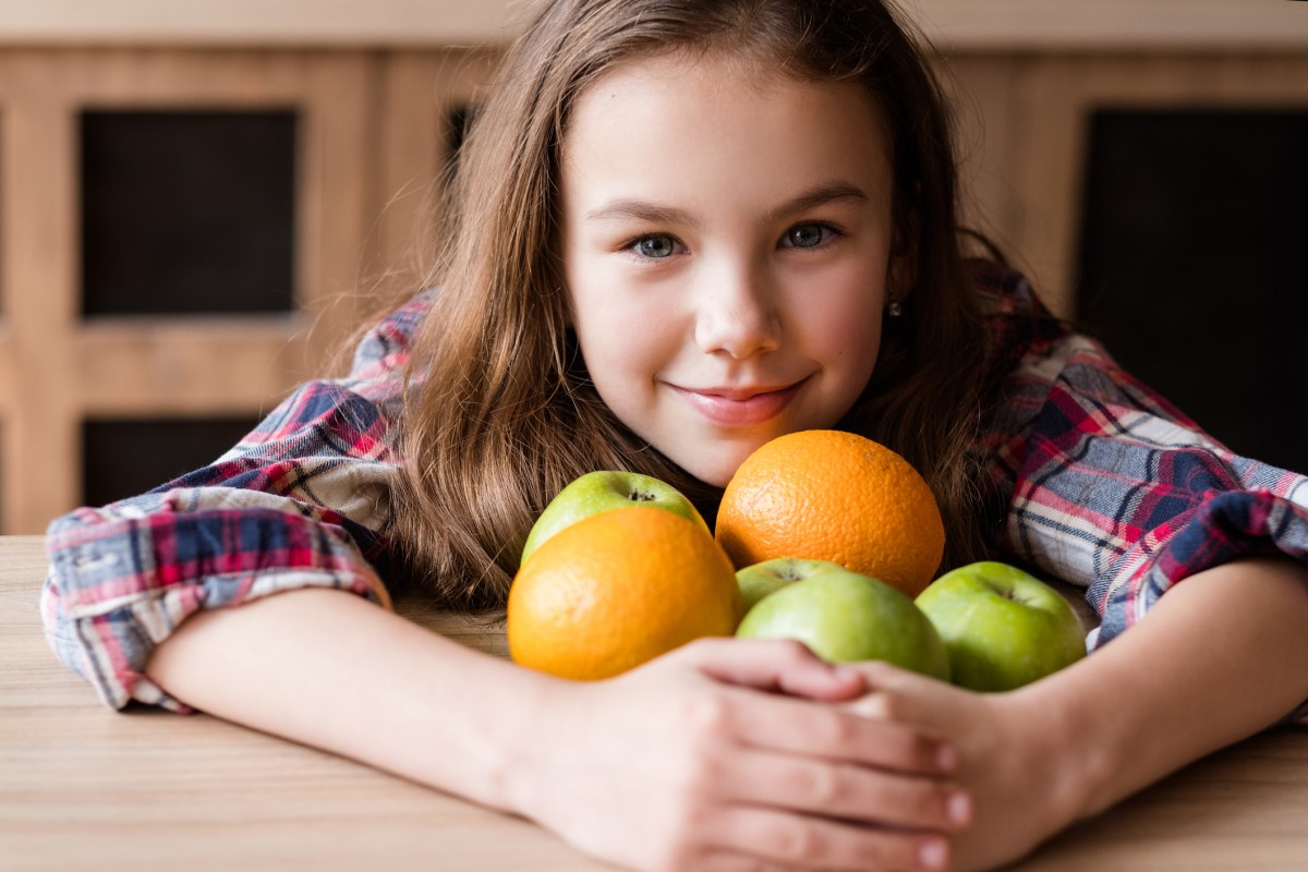 C vitamīns augļos, bērns ar apelsīniem un āboliem rokās.